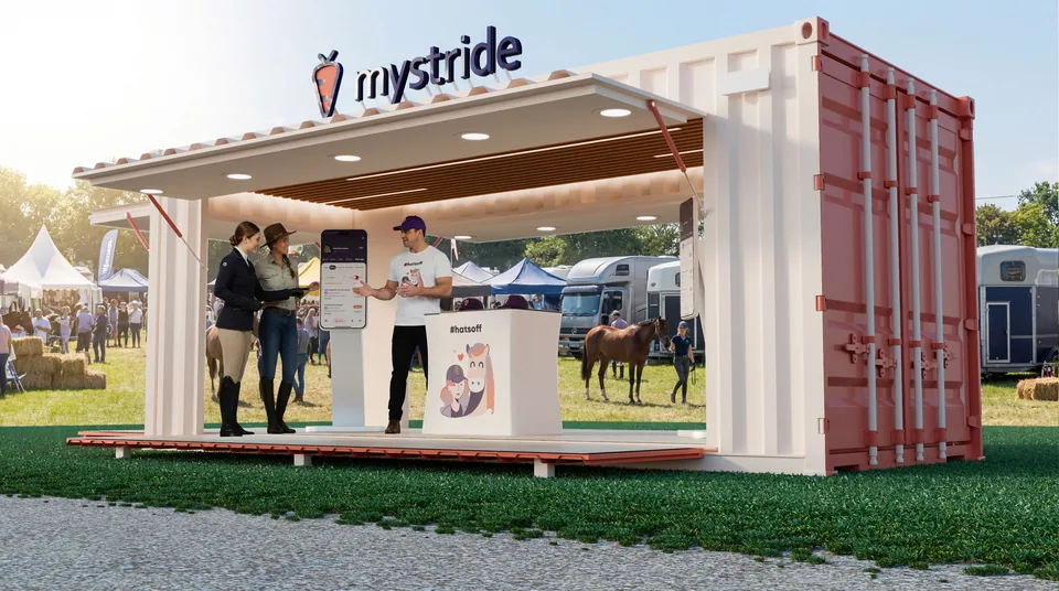 Close three-quarter 3D render of the MyStride container booth with staff at a phone kiosk and a busy horse show behind