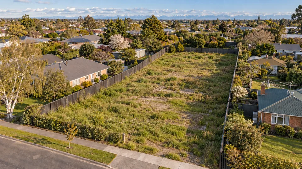 Vacant, overgrown residential section between older houses, seen from a drone-style viewpoint